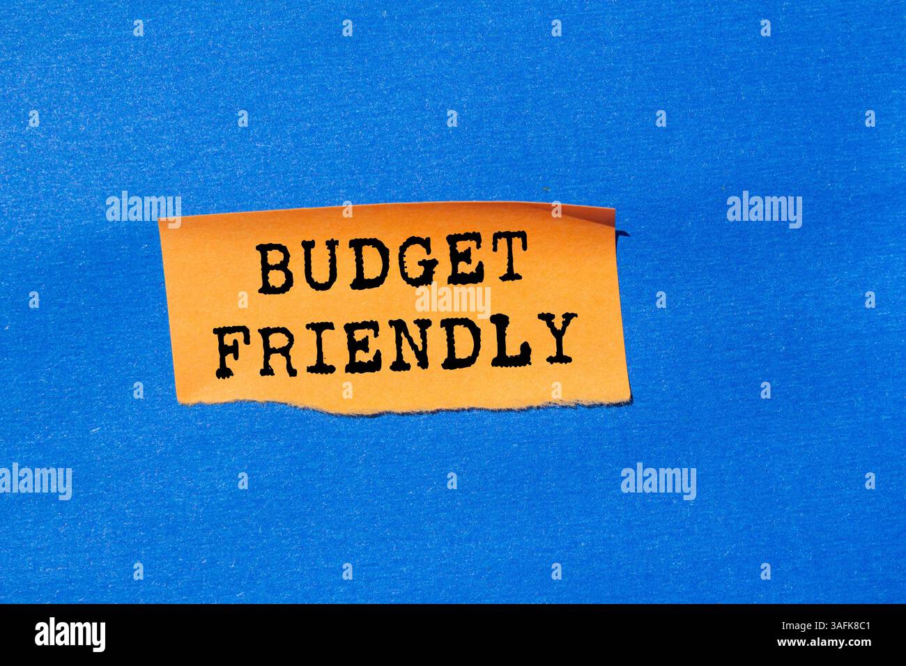 Messaggio economico scritto su carta arancione strappata su sfondo blu. Simbolo di budget concettuale. Copia spazio. Foto Stock