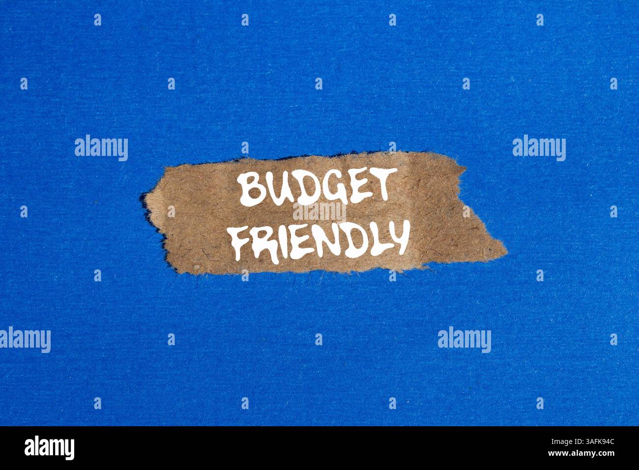Messaggio economico scritto su un pezzo di carta marrone strappato su sfondo blu. Simbolo di budget concettuale. Copia spazio. Foto Stock