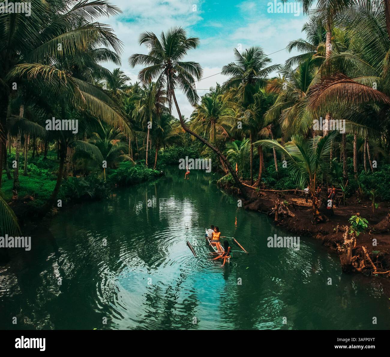 Vista aerea di un tranquillo fiume circondato da lussureggianti palme sull'isola di Siargao, Filippine, con una piccola barca che trasporta due persone Foto Stock