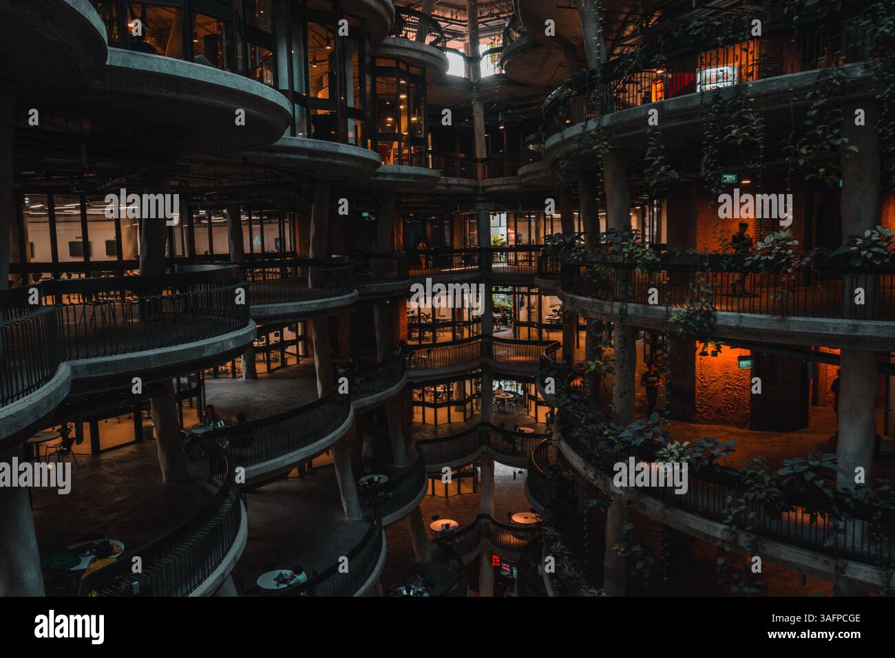 Didascalia: 'Elegante architettura moderna con balconi ricurvi su più livelli adornati da verde lussureggiante, che combinano innovazione e sostenibilità urbana Foto Stock