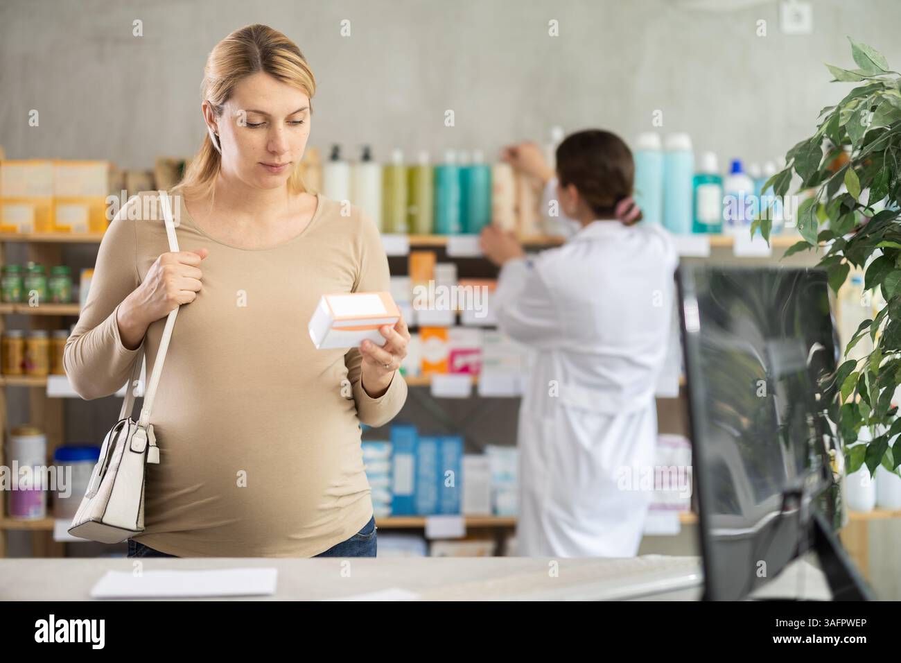Donna incinta scegliere pillole di integratori in farmacia, lavoro del personale in background Foto Stock