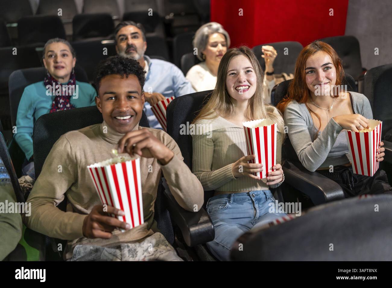 Gruppi di amici multietnici che si godono un film al cinema, condividono risate e sgranocchiano popcorn in un accogliente auditorium Foto Stock