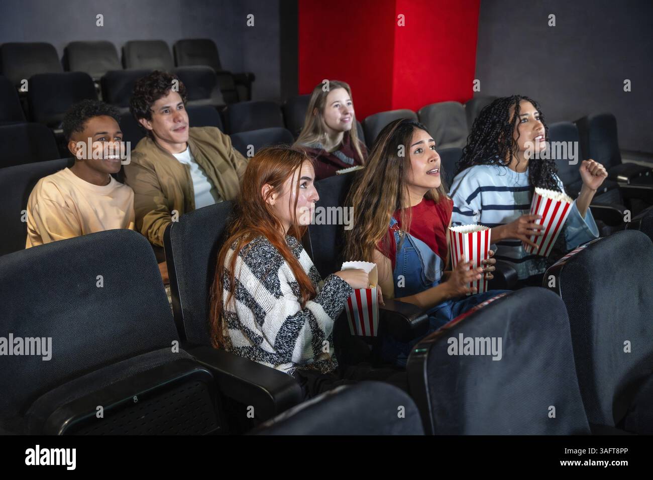 Gruppo di amici entusiasti che si godono un film e mangiano popcorn al cinema, condividendo un'esperienza divertente e divertente Foto Stock
