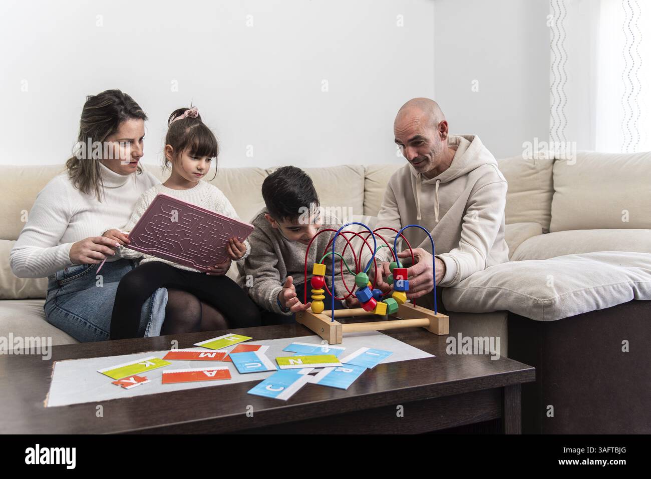 La famiglia si diverte insieme sul divano, giocando con giocattoli educativi e imparando l'alfabeto Foto Stock