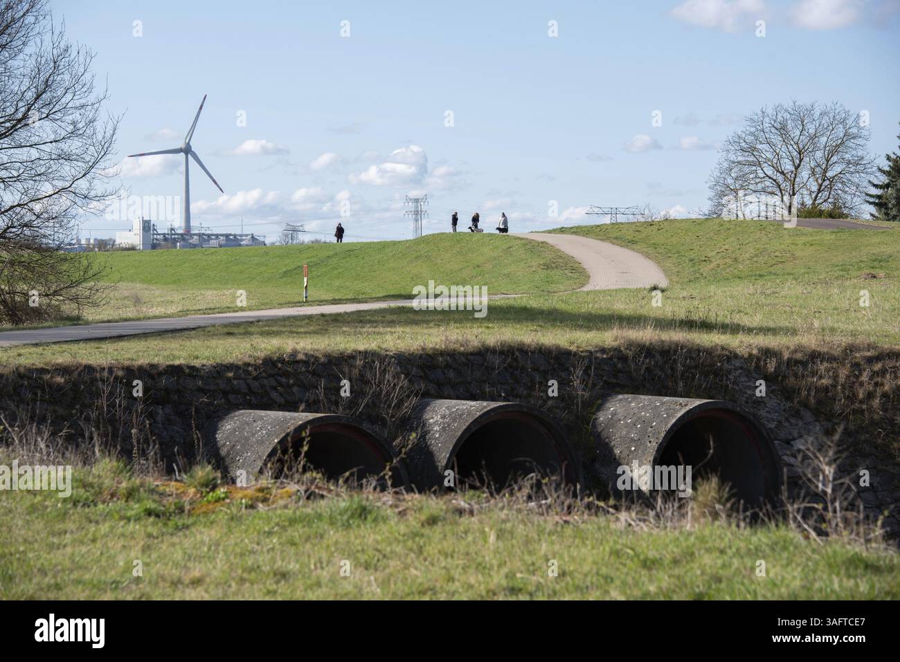 Scenario rurale con camminatori su un sentiero collinare, turbine eoliche sullo sfondo e un ponte con tubi d'acqua in primo piano, Glindenberg, Sassonia-Anhalt, G. Foto Stock