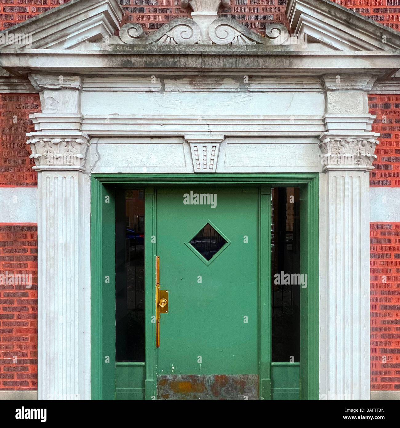Elegante porta verde con finestra a forma di diamante posta in un'entrata in pietra neoclassica riccamente dettagliata su un edificio in mattoni rossi a Chicago - Immagine stock catturata con smartphone