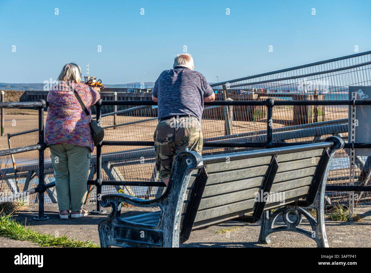 Un uomo e una donna stanno insieme ammirando la vista sul porto di Burry Port nel Carmarthenshire, Galles del Sud, Regno Unito, in un giorno di primavera di sole Foto Stock