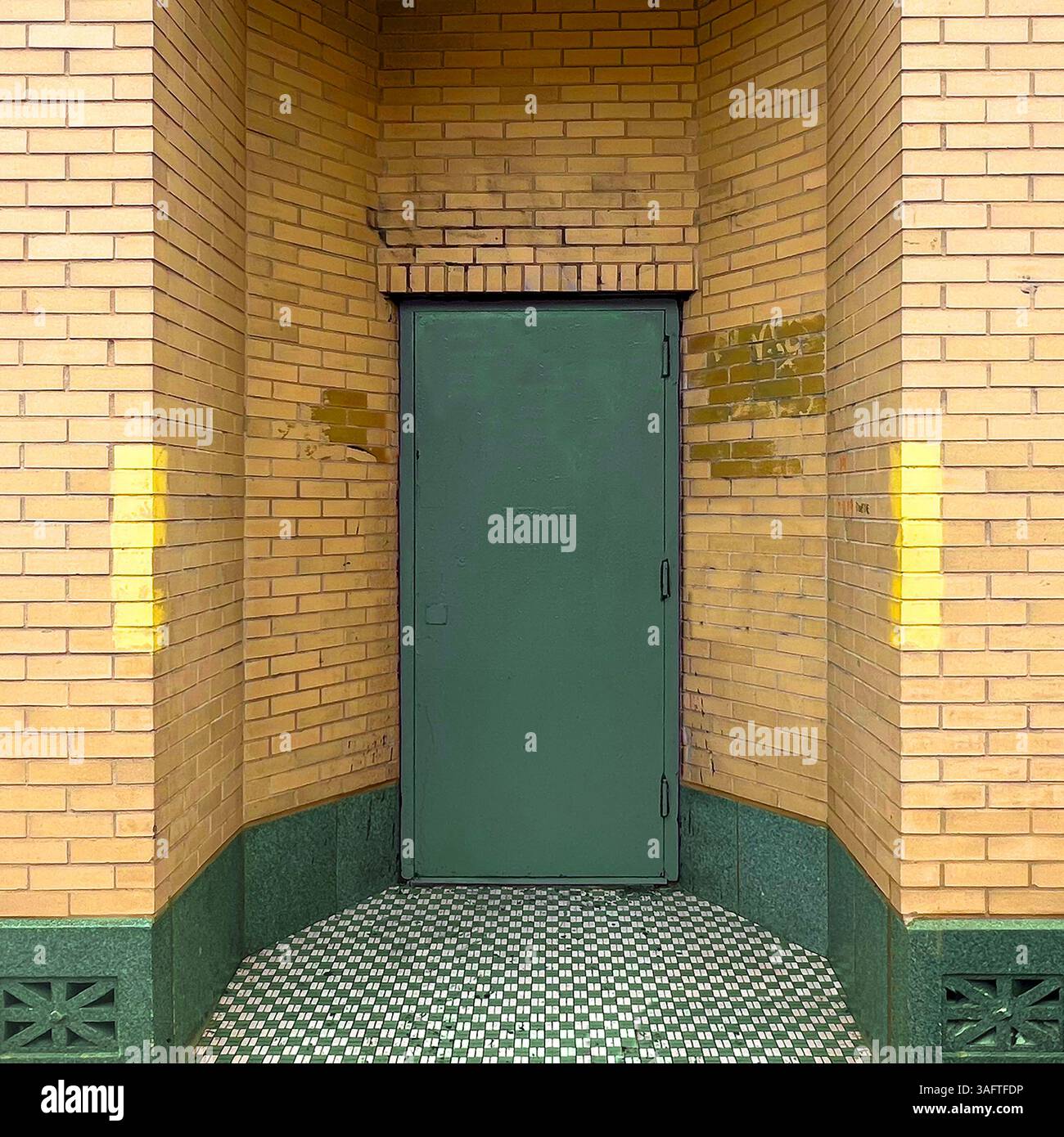 Porta in acciaio verde adagiata in un angolo di mattoni gialli con base piastrellata verde e pavimento a scacchi in mosaico in un ingresso di un edificio industriale di Chicago - Immagine stock catturata con smartphone
