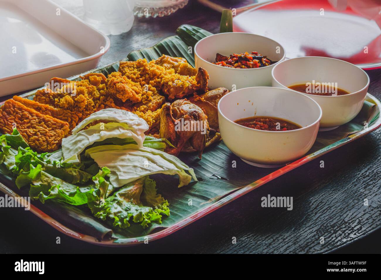 Una porzione di pollo fritto croccante accompagnato da tempeh, lattuga, cavolo, salse e sambal, un piatto popolare in stile sundanese di indones Foto Stock