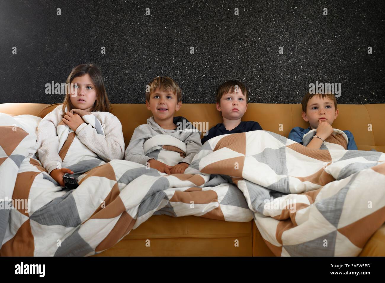 I bambini si siedono vicini davanti a un televisore, i loro volti si illuminano di espressioni mutevoli: Gioia, meraviglia, paura, sorpresa ed eccitazione Foto Stock
