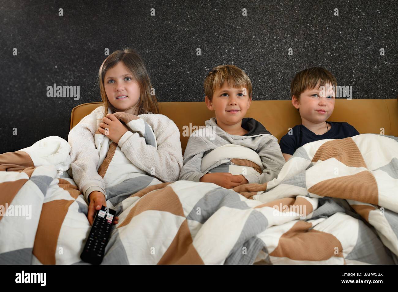 I bambini si siedono vicini davanti a un televisore, i loro volti si illuminano di espressioni mutevoli: Gioia, meraviglia, paura, sorpresa ed eccitazione Foto Stock