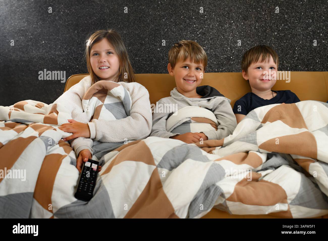 I bambini si siedono vicini davanti a un televisore, i loro volti si illuminano di espressioni mutevoli: Gioia, meraviglia, paura, sorpresa ed eccitazione Foto Stock