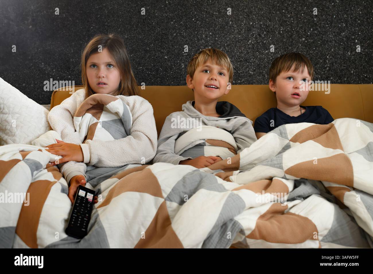 I bambini si siedono vicini davanti a un televisore, i loro volti si illuminano di espressioni mutevoli: Gioia, meraviglia, paura, sorpresa ed eccitazione Foto Stock