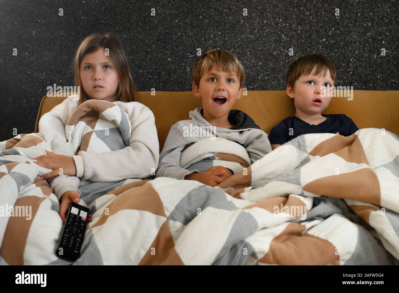 I bambini si siedono vicini davanti a un televisore, i loro volti si illuminano di espressioni mutevoli: Gioia, meraviglia, paura, sorpresa ed eccitazione Foto Stock