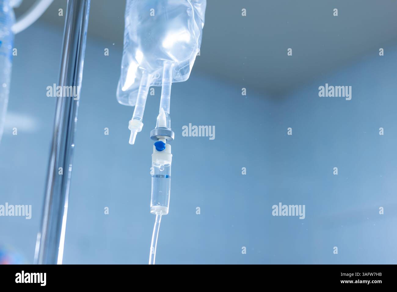 Primo piano del sistema di infusione IV con sacca di liquido trasparente in ambiente ospedaliero, utilizzato per l'idratazione e il trattamento dei pazienti. Foto Stock