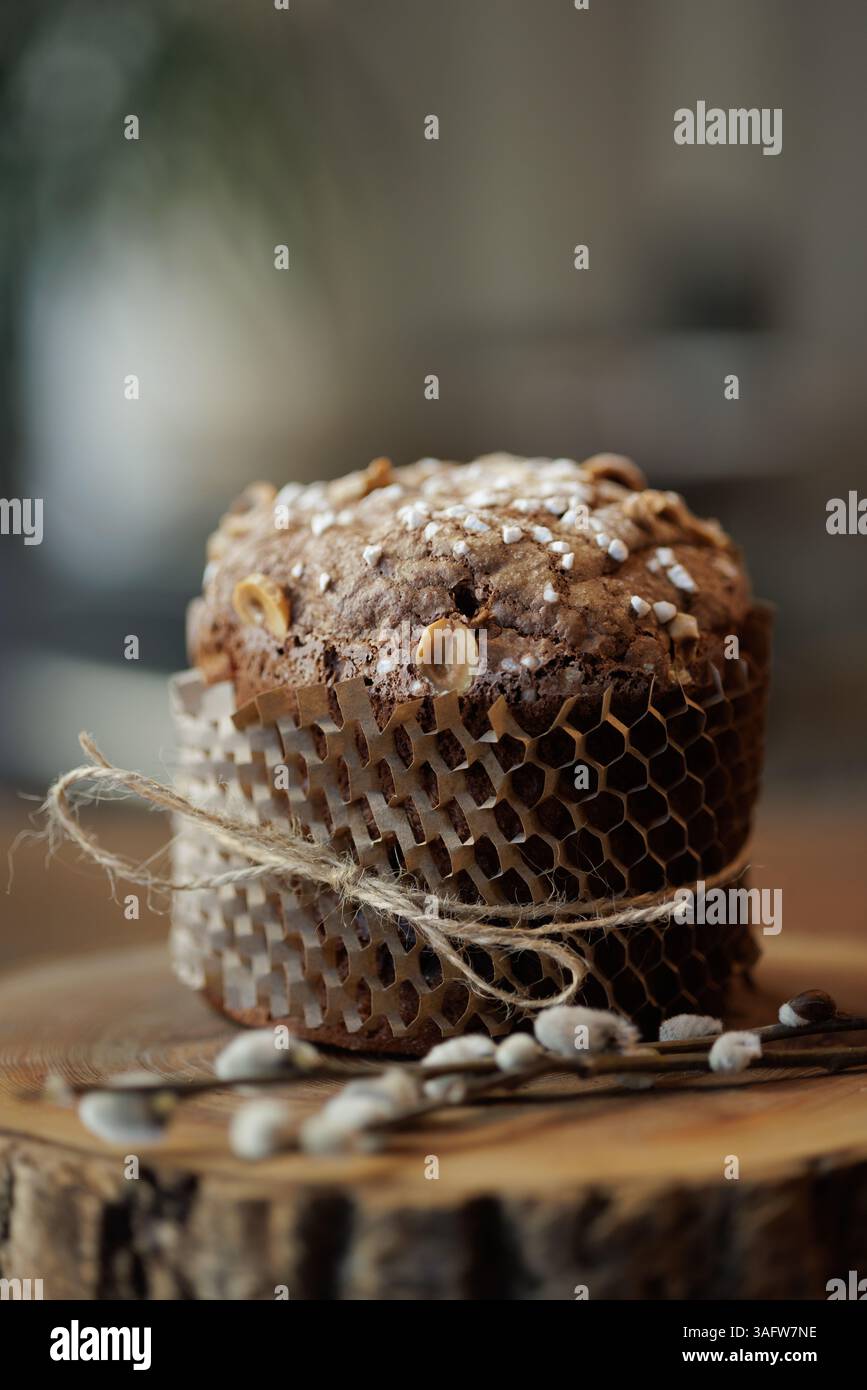 Torta pasquale al cioccolato artigianale con nocciole e zucchero, avvolta in carta ecologica su una lastra di legno rustica. Foto Stock