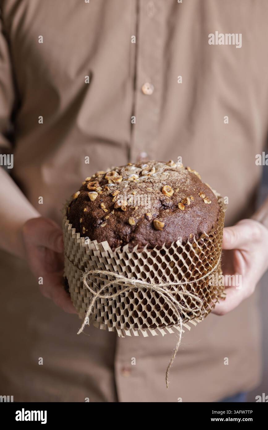 Uomo che tiene in mano la tradizionale torta pasquale al cioccolato con nocciole in un involucro di carta ecocompatibile per le feste. Foto Stock