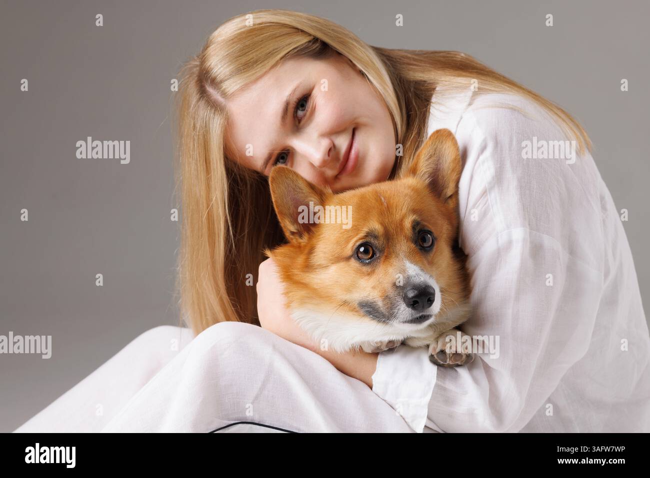 Una donna bionda abbraccia amorevolmente il suo cane Corgi seduto, sia con un aspetto calmo che connesso in un momento caldo. Foto Stock