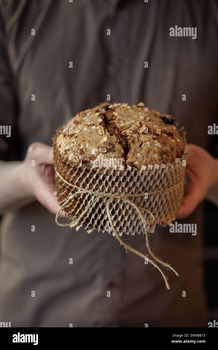 Uomo che tiene in mano pane pasquale artigianale con mandorle e zucchero, avvolto in carta kraft ecologica per regali. Foto Stock
