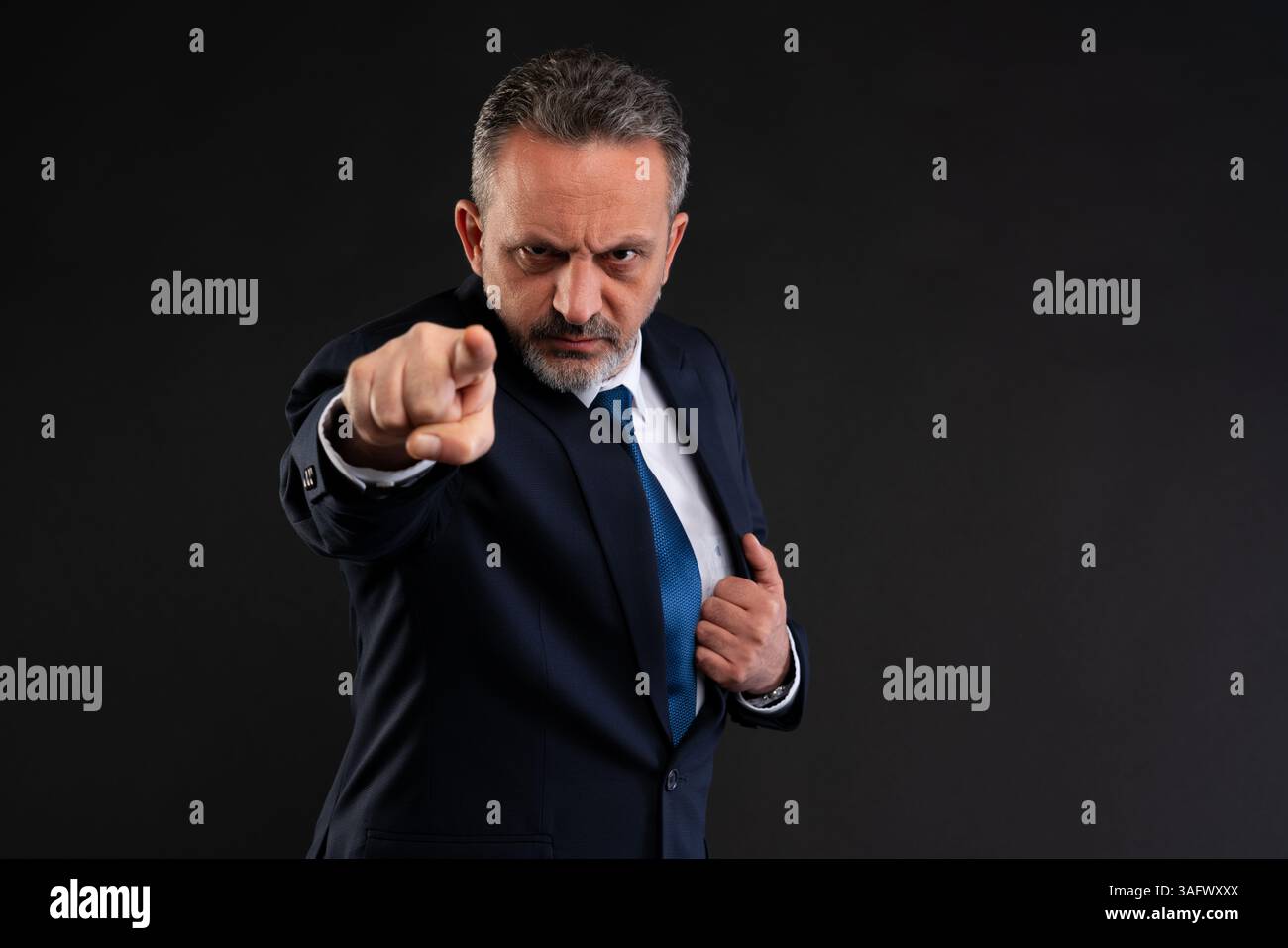 Uomo d'affari maturo in tuta con un'intensa espressione che punta in avanti, trasmette autorità, leadership, responsabilità o comunicazione diretta. Foto Stock