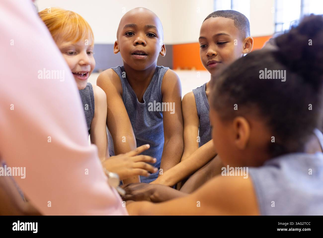 Nella palestra scolastica, bambini diversi in divise sportive che si uniscono e discutono del lavoro di squadra Foto Stock
