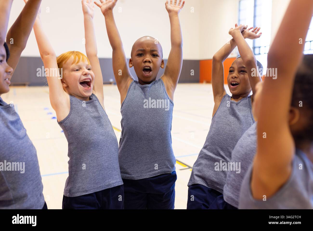 Nella palestra scolastica, bambini diversi che fanno il tifo e alzano le mani, godendo di lezioni di educazione fisica Foto Stock
