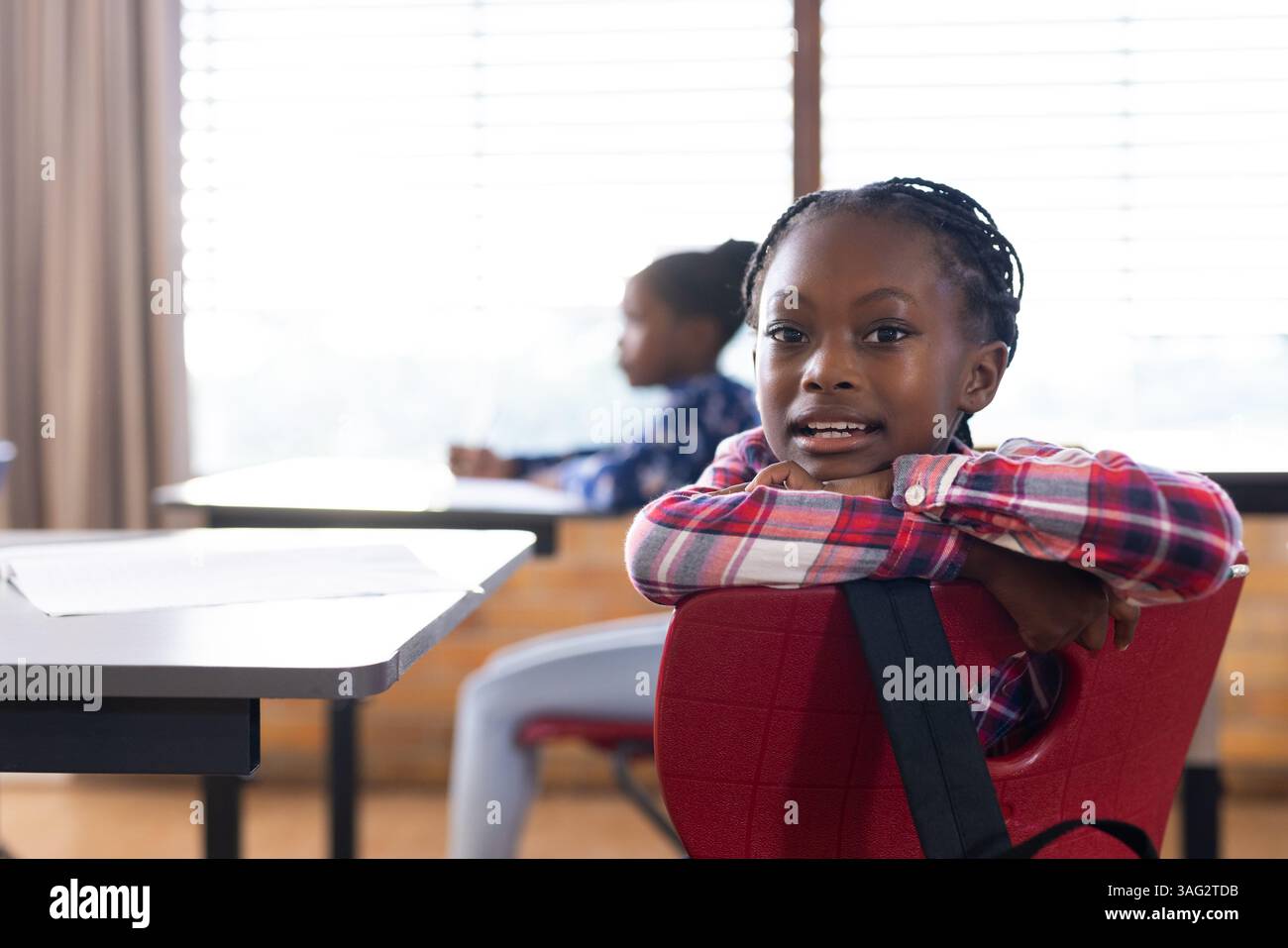 A scuola, ragazza afroamericana seduta alla scrivania e sorridente, godendo dell'ambiente in classe Foto Stock
