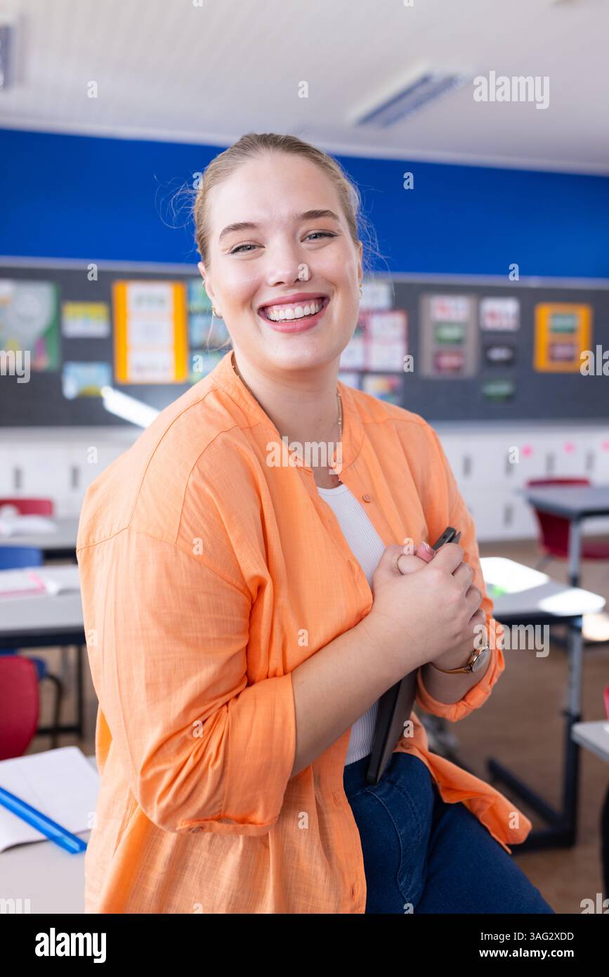 Professoressa sorridente che tiene un tablet in classe, pronta per la lezione scolastica Foto Stock