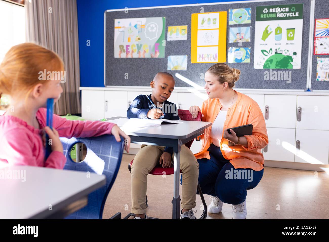 Aiutare un ragazzo afroamericano con un tablet a scuola, un'insegnante donna e un altro studente a guardare Foto Stock