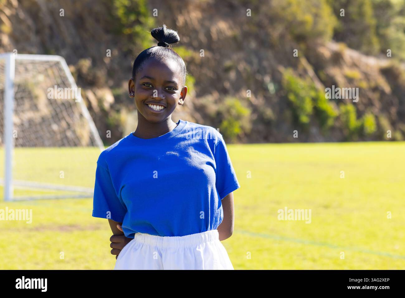 Sorridente ragazza afroamericana in uniforme sportiva in piedi sul campo di calcio a scuola, copia spazio Foto Stock