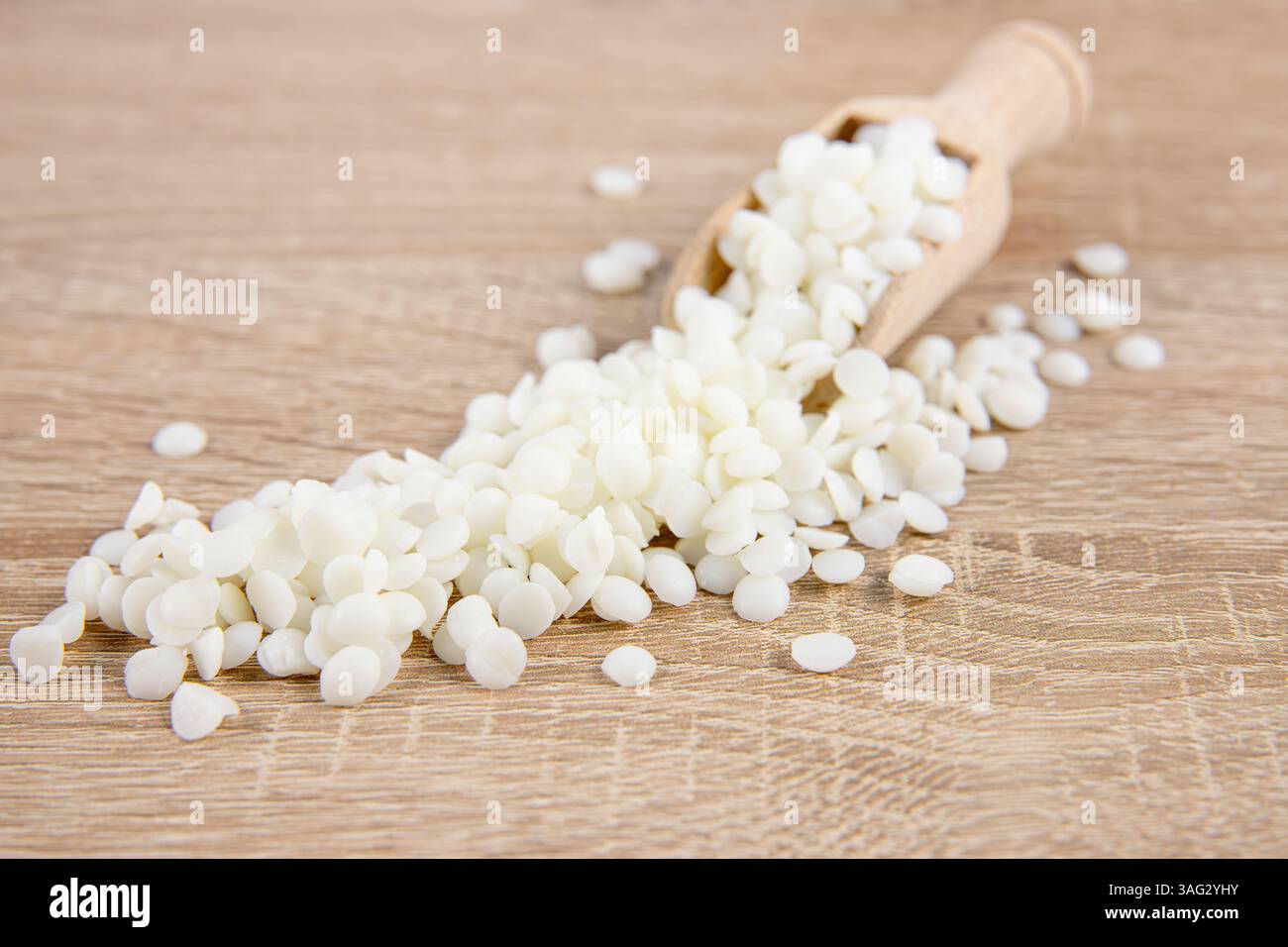 Pellet di cera di soia su paletta in legno, sparsi su un tavolo in legno, foto in studio, interni. Materiale pulito e sostenibile per la produzione di candele. Foto Stock