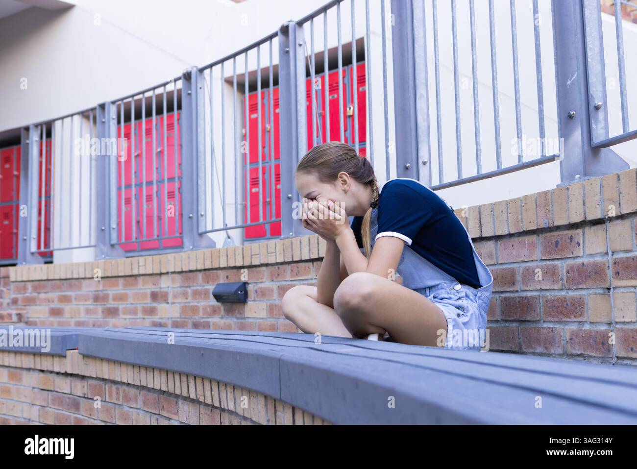 Seduta da sola, ragazza che piange con le mani che coprono il viso a scuola Foto Stock