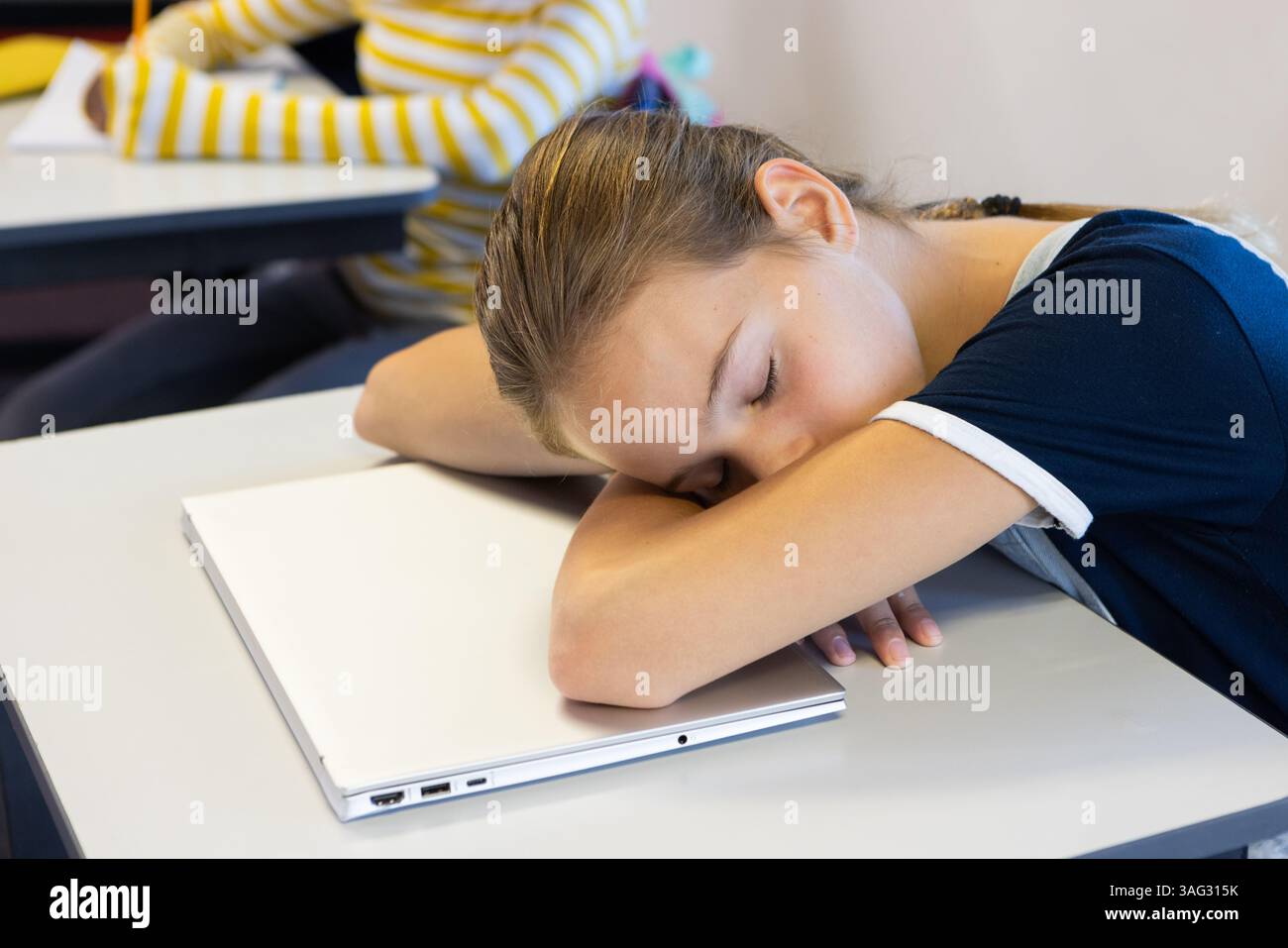 Dormi sulla scrivania con un portatile, mentre una ragazza in classe durante la lezione Foto Stock