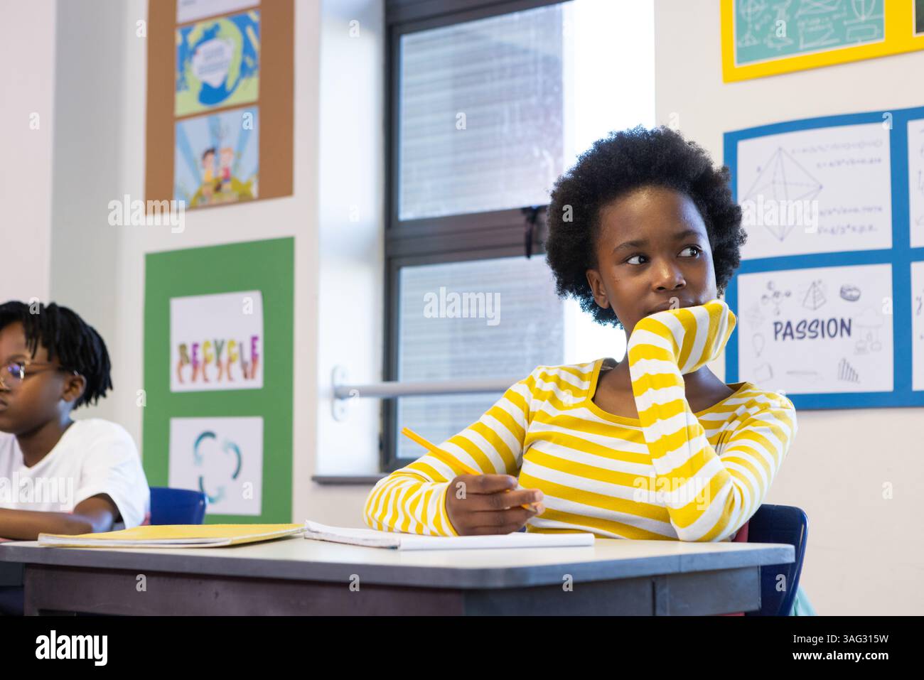 A scuola, ragazza afroamericana in camicia a righe sognando ad occhi aperti mentre tiene la matita in classe Foto Stock