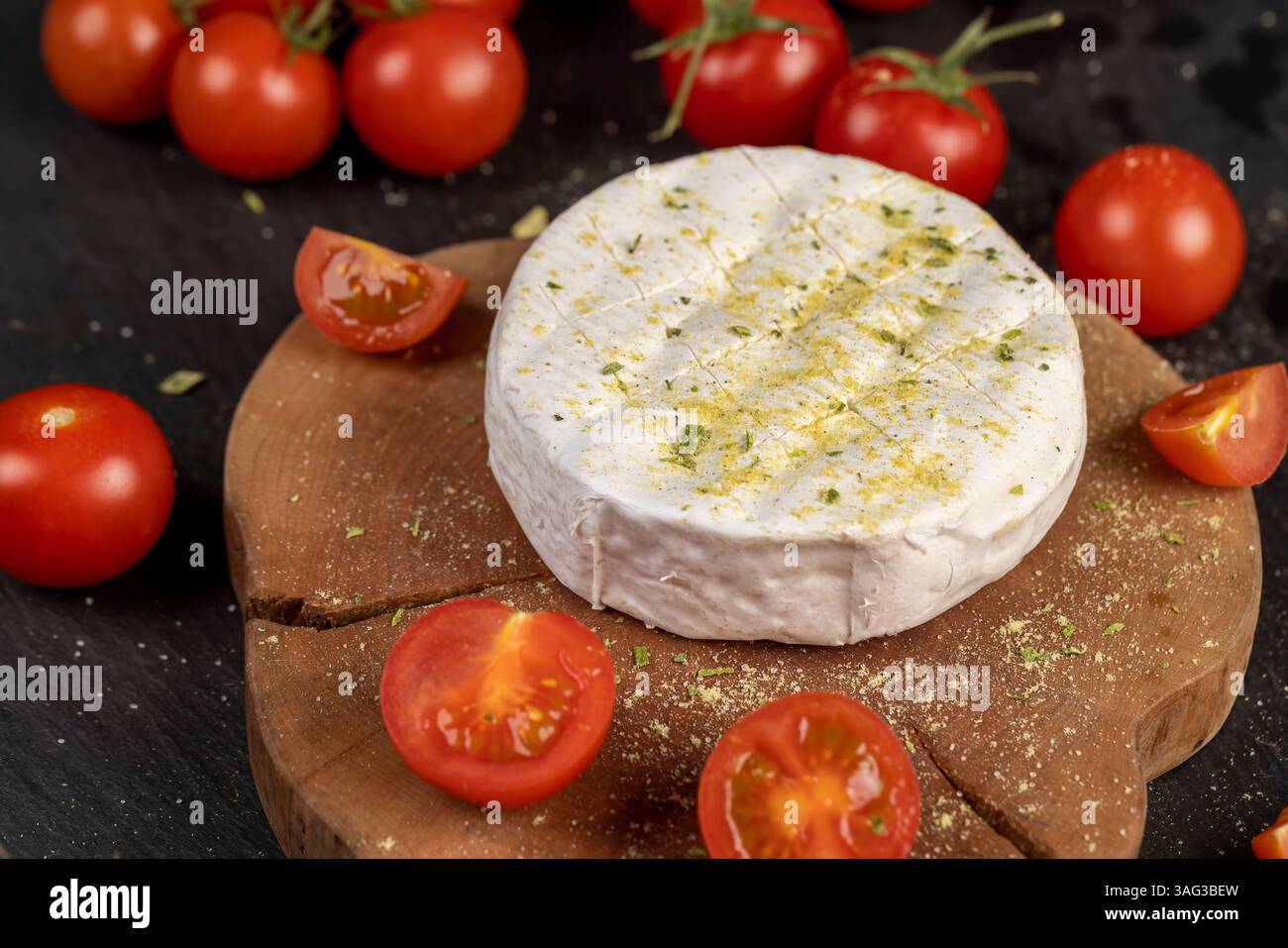 formaggio morbido con muffa cosparsa di spezie e piccoli pomodori rossi maturi, formaggio morbido bianco con sale e spezie e pomodori rotondi rossi piccoli sul tabl Foto Stock