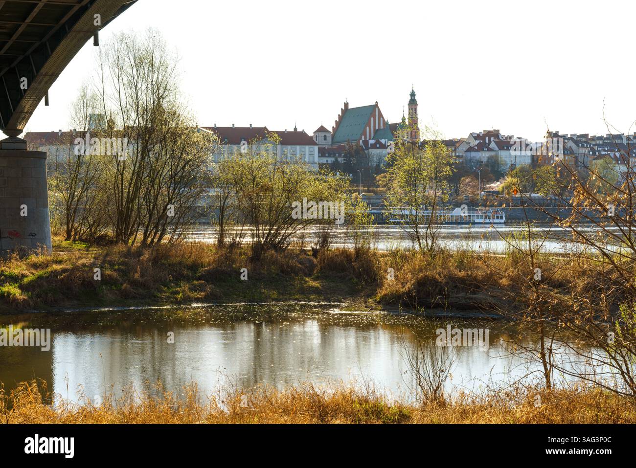 Warszawa, città vecchia ricostruita, castello reale visto dall'altro lato della Vistola attraverso le rive verdi del fiume. Serata di sole sotto il ponte. Foto Stock