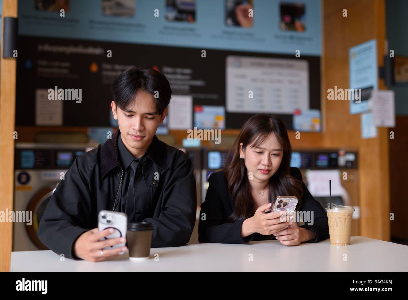 Giovane coppia asiatica felice seduta in lavanderia a bere caffè e a usare il telefono Foto Stock