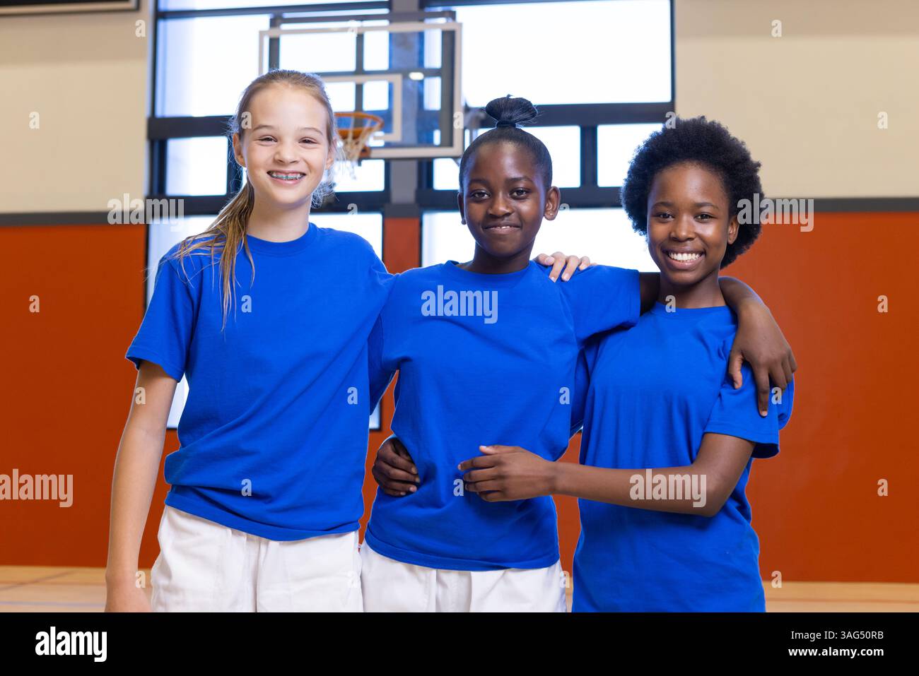 Sorridere diverse ragazze nella palestra scolastica indossando camicie blu, posare per la foto di gruppo Foto Stock