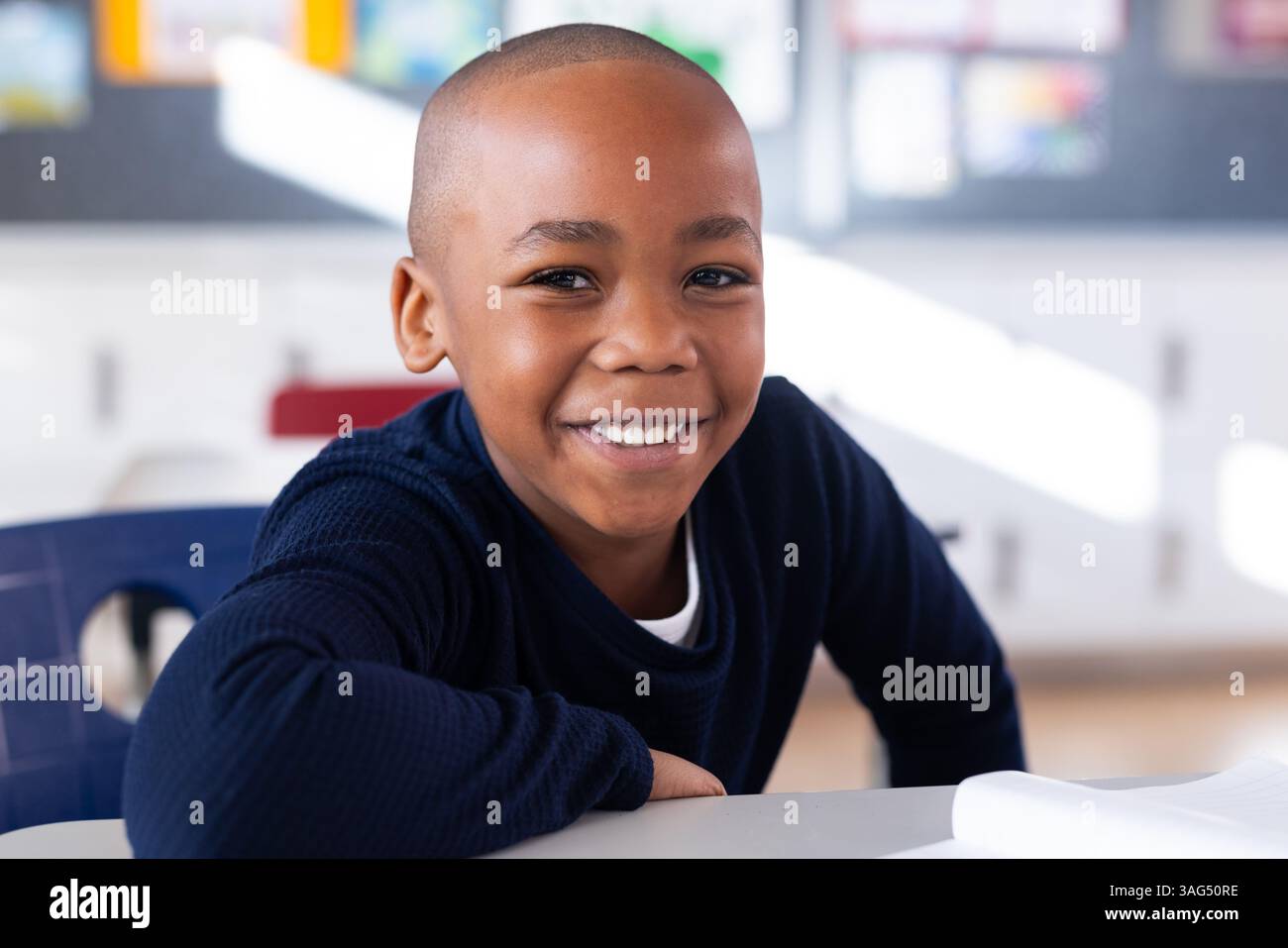 Sorridente ragazzo afroamericano seduto alla scrivania in classe a guardare la macchina fotografica Foto Stock