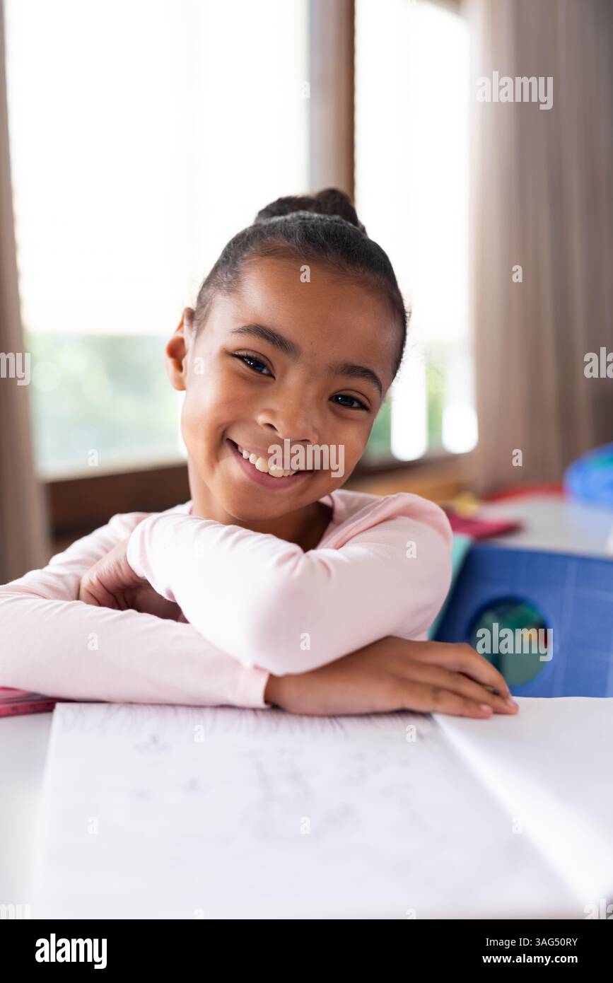 Ragazza sorridente a scuola appoggiata sulla scrivania con la carta, godendo del tempo in classe Foto Stock