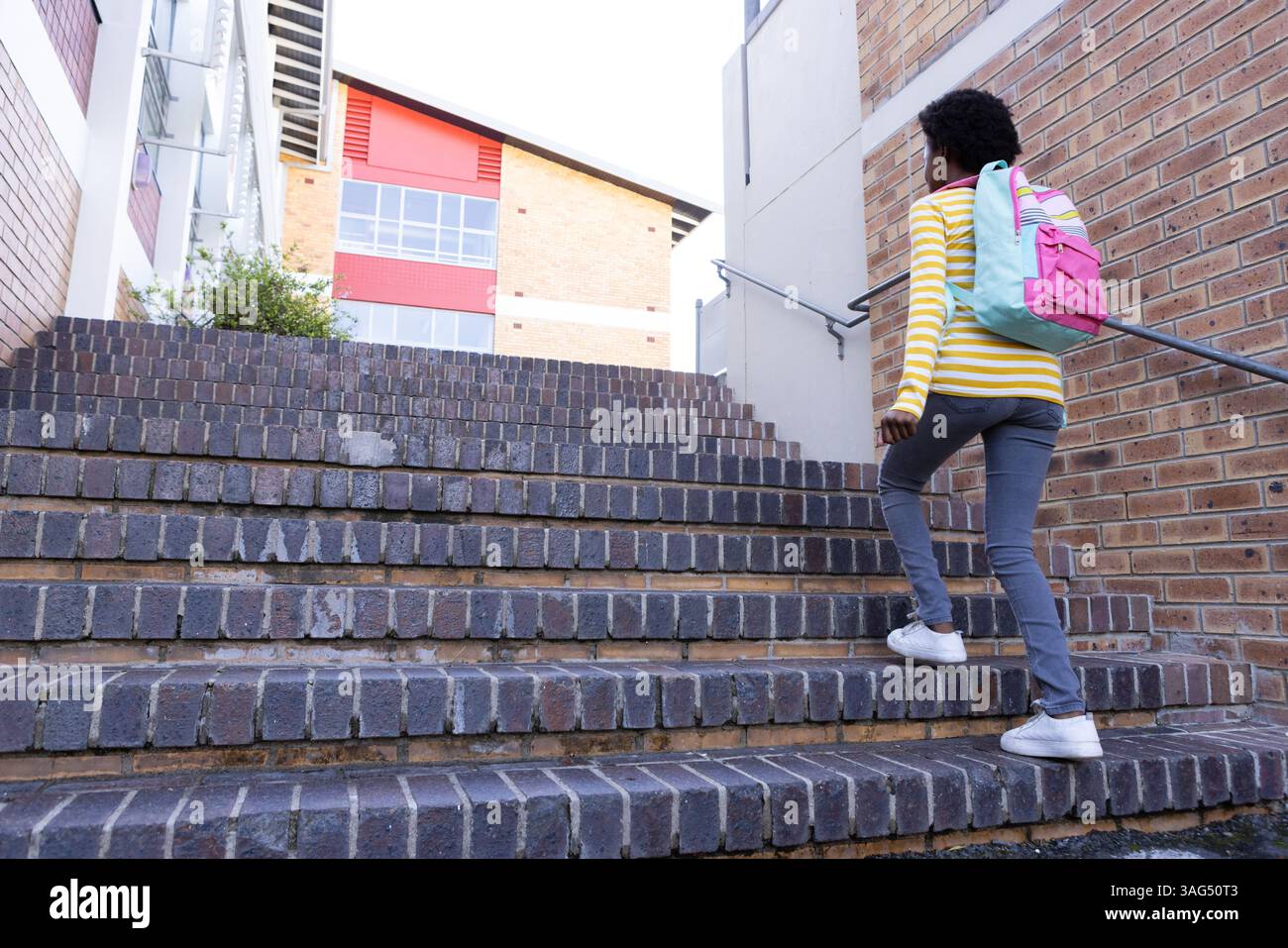 Salendo le scale, ragazza afroamericana con zaino che va all'edificio scolastico Foto Stock