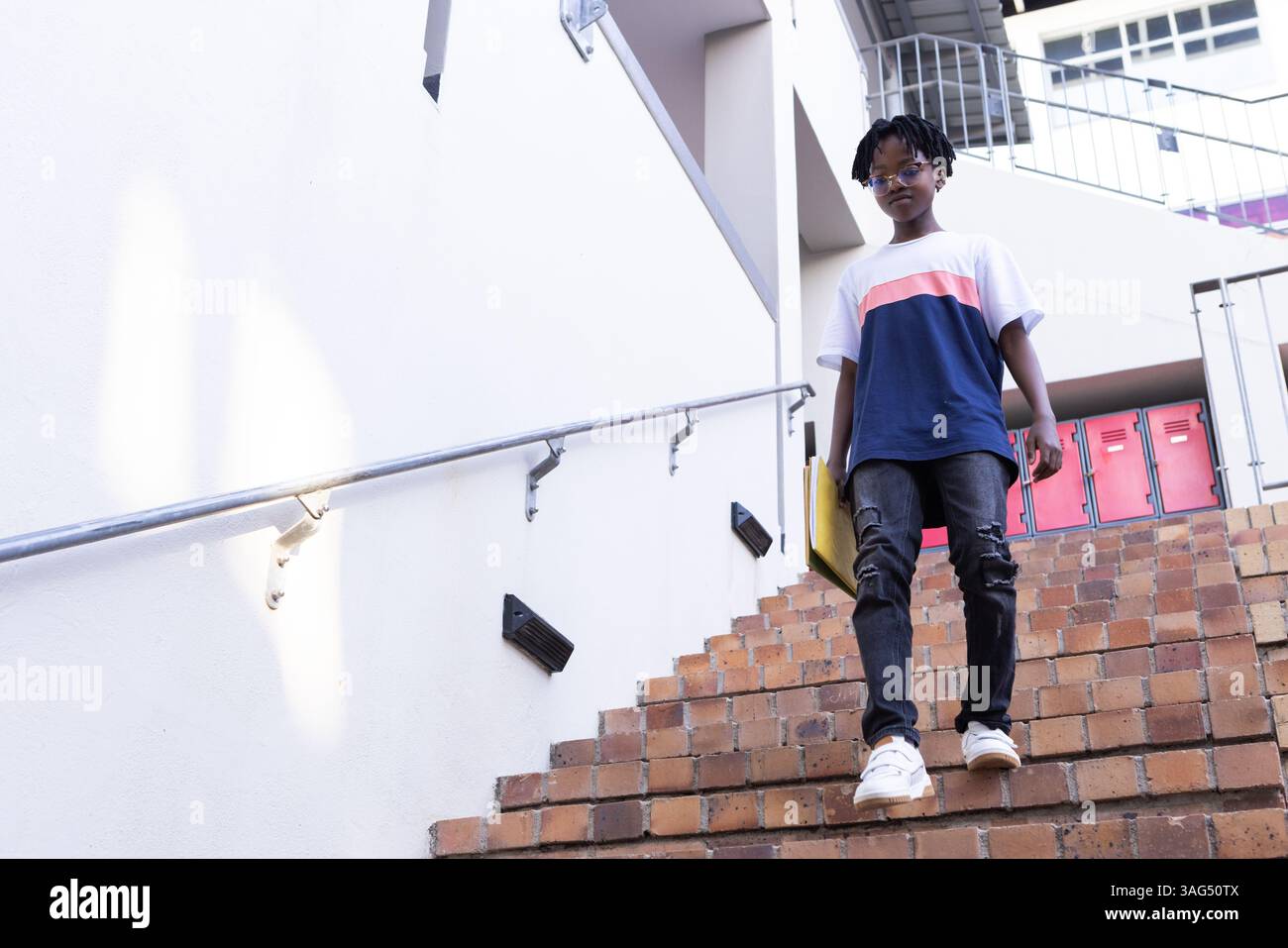 Scendendo le scale, ragazzo afroamericano in abiti casual a scuola, che sembra sicuro di sé Foto Stock