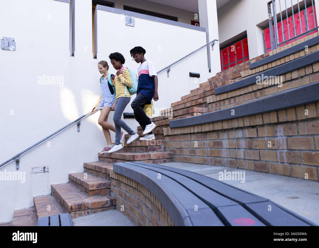 Scendendo le scale, tre bambini diversi della scuola che parlano e tengono i quaderni Foto Stock