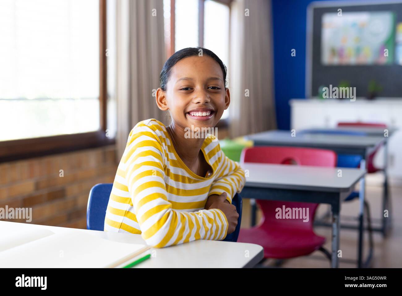 Ragazza sorridente seduta alla scrivania in classe, godendo dell'ambiente scolastico Foto Stock
