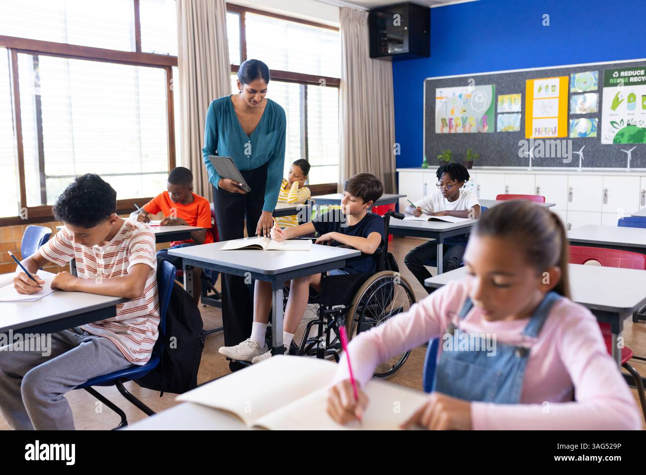 Insegnante femminile indiana che assiste gli studenti in classe, diversi gruppi che studiano a scuola Foto Stock