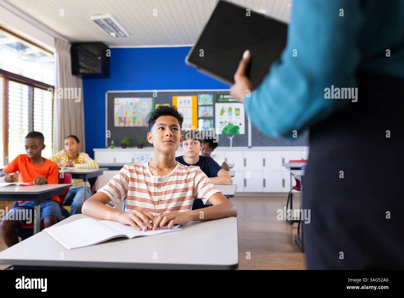 A scuola, gli studenti seduti alle scrivanie ascoltano un'insegnante indiana che tiene un tablet Foto Stock