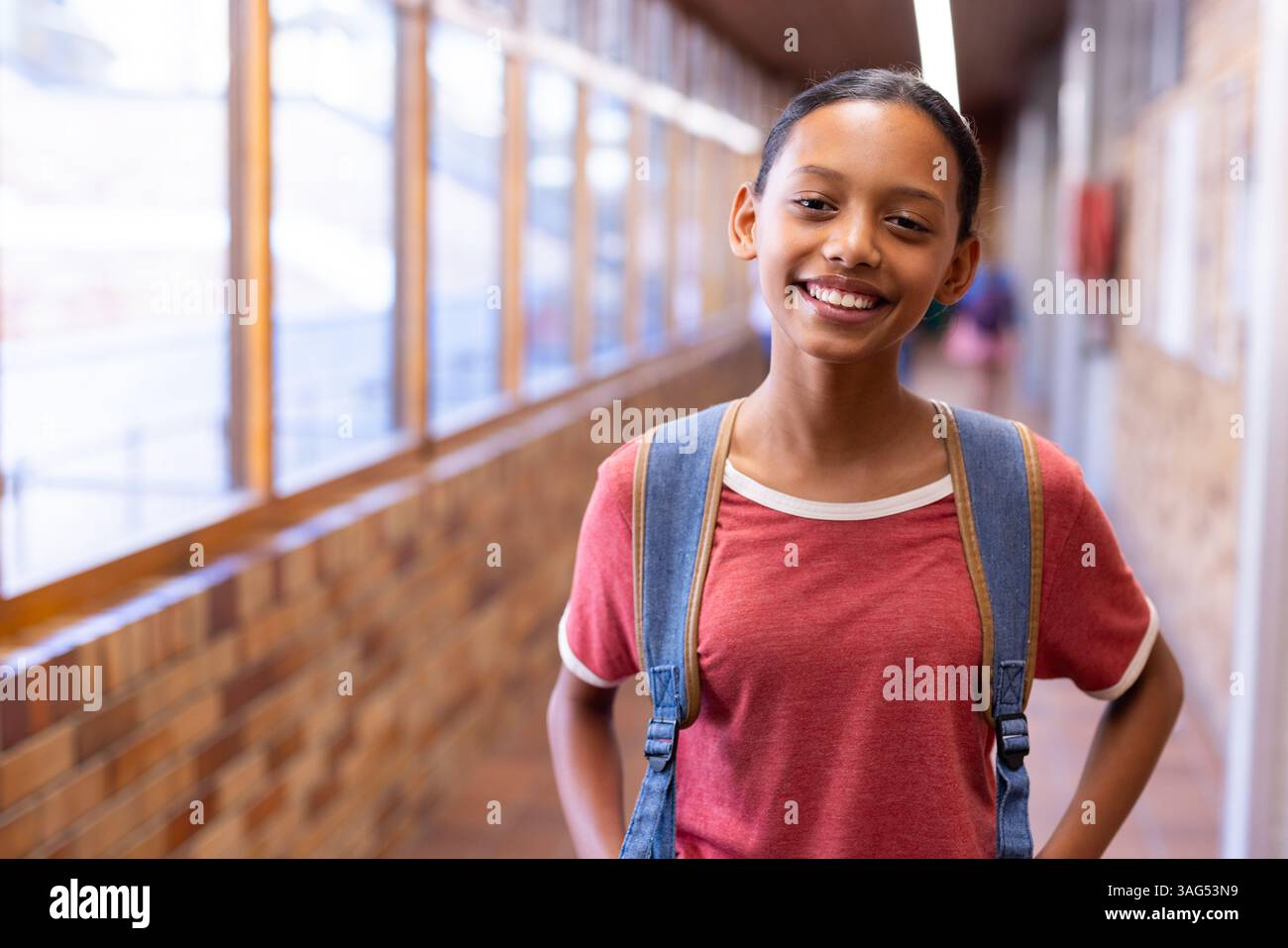 Studente sorridente con zaino in piedi nel corridoio della scuola, che sembra sicuro di sé Foto Stock