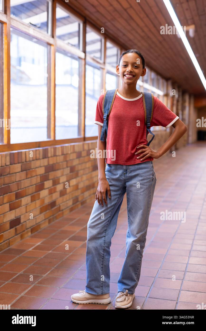 Studente sorridente con zaino in piedi nel corridoio della scuola, che posa con fiducia Foto Stock