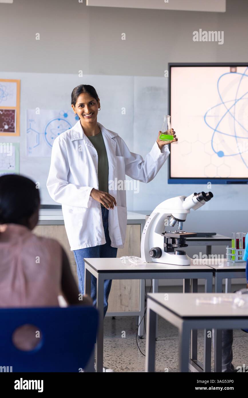 A scuola, insegnante indiana che tiene la fiasca e spiega agli studenti l'esperimento scientifico Foto Stock