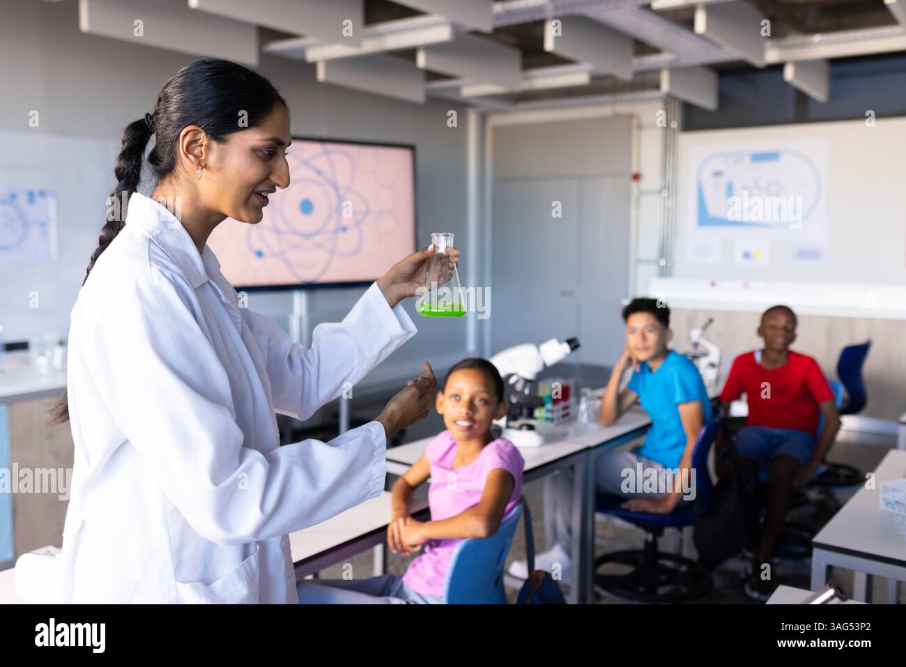 A scuola, insegnante indiana che tiene in mano la fiasca con liquido verde, gli studenti guardano attentamente Foto Stock